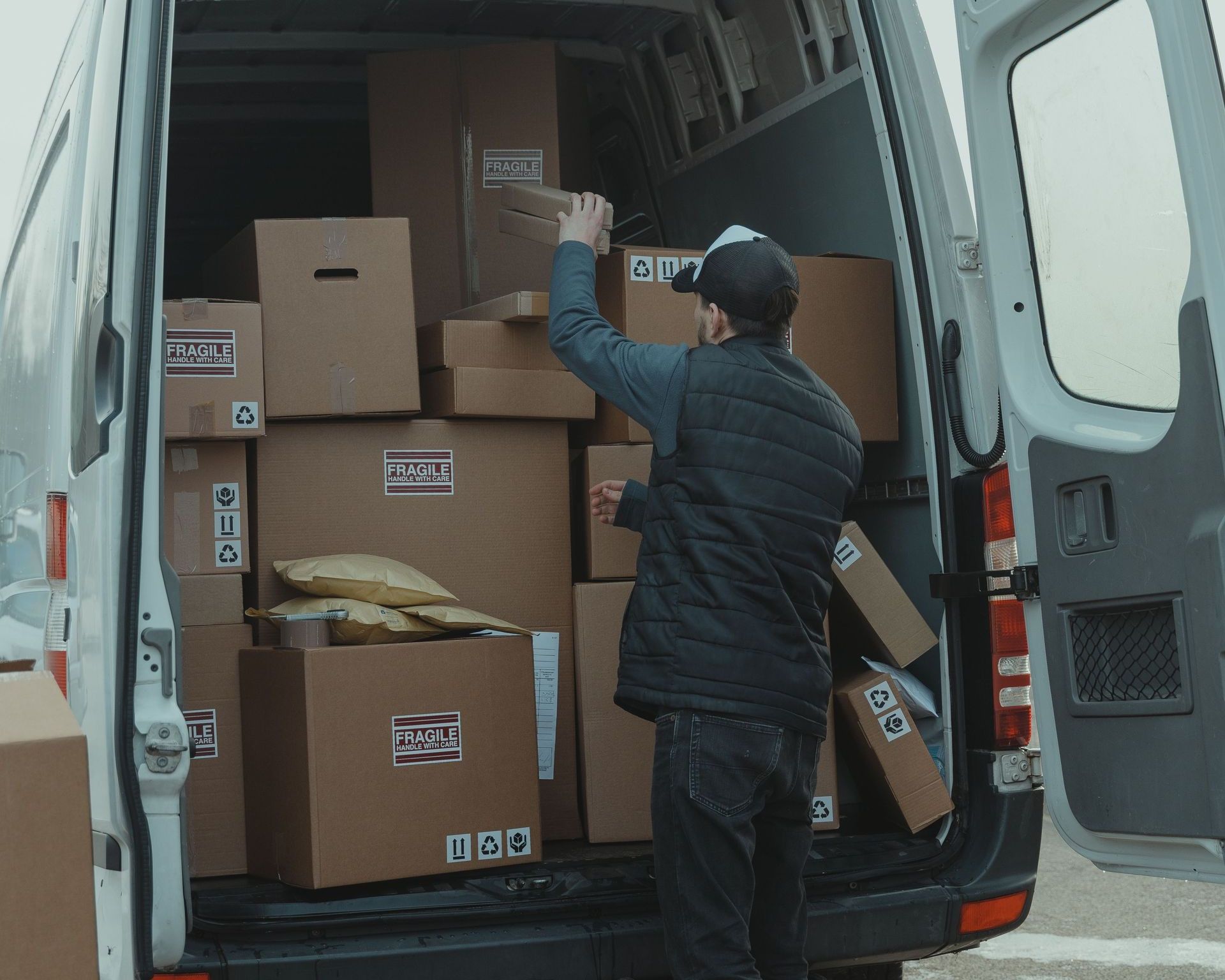 A courier organizing boxes in a delivery van for shipment on a cloudy day.