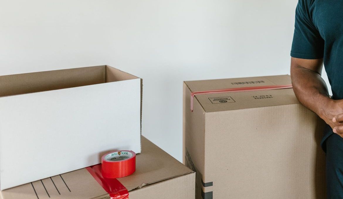 A cheerful man with afro hair standing next to moving boxes indoors, smiling.