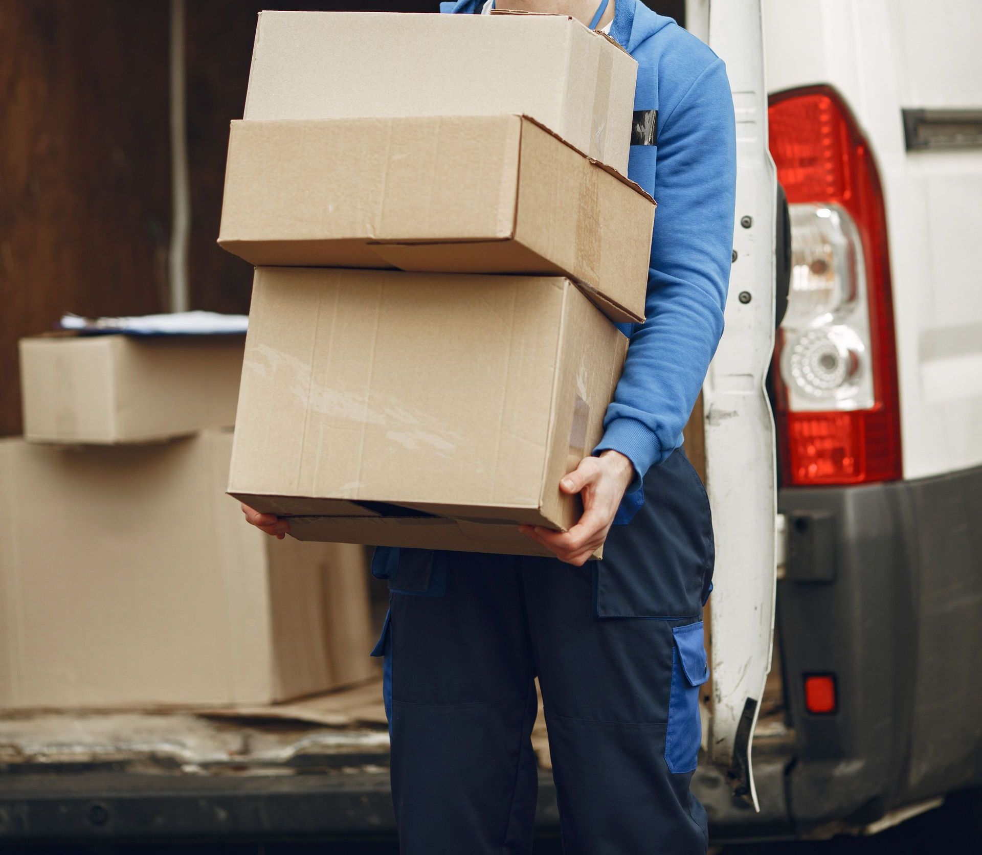 Man wearing mask delivering cardboard boxes from van outdoors.